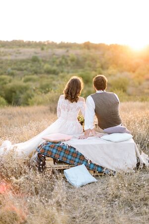 back view of young couple sitting in a field and watching the sunset . outdoor weddingの写真素材