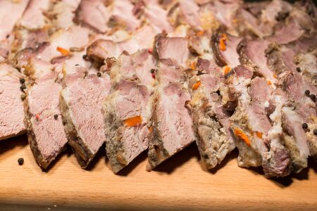 baked pork stuffed with carrots, sliced into thin slices on a wooden board. juicy slices of cooked meat close-up.の写真素材