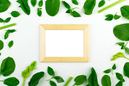 Fresh green vegetables and herbs set on a white background around an empty frame.の写真素材