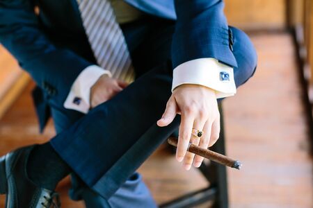 big boss style, masculinity concept. close-up of the hand of a young businessman smoking cigar and sitting on a chair.の写真素材