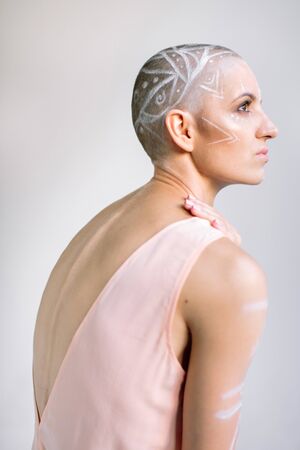 Side view of female with painted ornament on shaved head touching shoulder and looking away against...