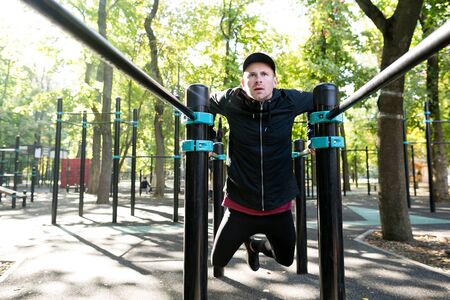 Focused sportive man doing parallel bars dips looking forward and working out in green park