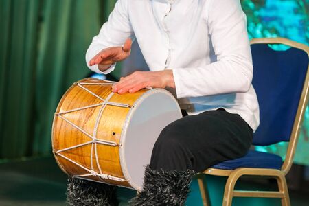 Crop of a caucasian man in a ethnic costume sits on a chair and plays the drum with his hands. Music...