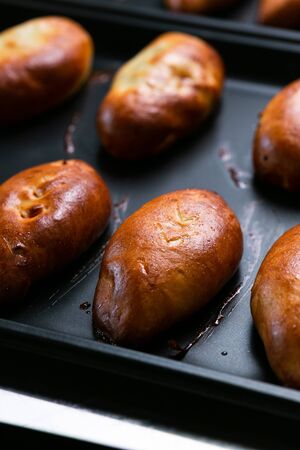 Ready golden pies on pan sheet. Arranged stuffed pies with golden crust on metal baking sheetの写真素材