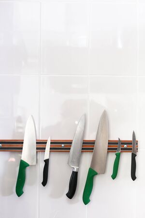 Magnetic strip with collection of knives. Hanging magnetic strip with set of sharp knives on white...