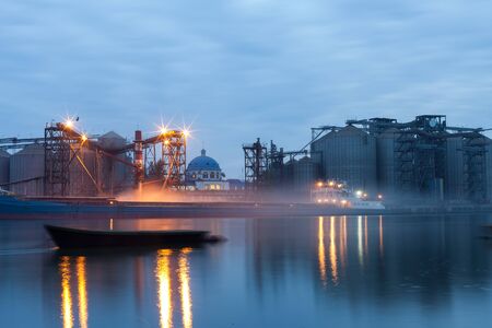 the process ofLoading cargo barges at the river port at night on a long shutter speed. The illuminated urban landscape in the reflection of the riverの写真素材