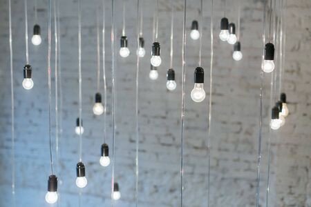 Set of incandescent lamp bulb hanging from the wall against a white brick wall. Large decorative art of lightning. Home decoration concept.の写真素材