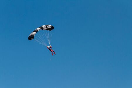 Human silhouette running a colorful parachute in the blue sky without clouds. Copy pastre space