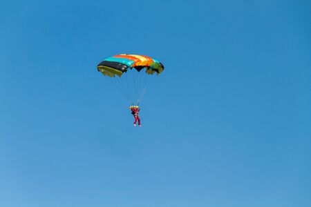 Man soaring in the air currents on a colored parachute against a background of blue.の写真素材