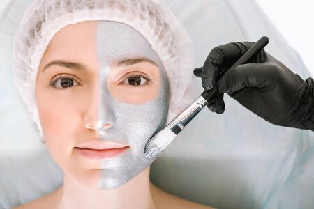 Nice woman looks directly into the camera while lying on a cosmetology table and applying a silver...