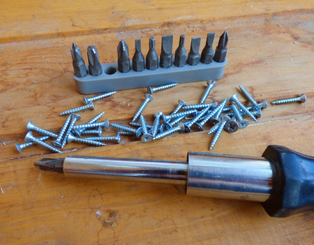 Screws, screwdriver and set of bits (heads) on wood background. Home improvement tools and...
