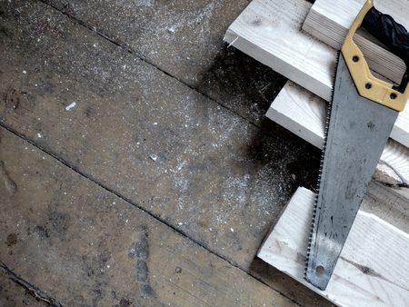 New fresh boards and saw on aged wooden surface (floor or table). Abstract background. Natural materials - two kinds of wood. Filtered, desaturated.の写真素材