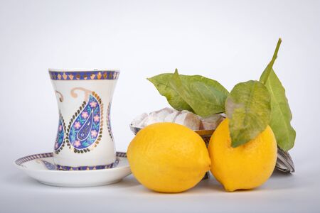 Traditional white color  armudu tea Cup with national patterns and buta print. Two lemons with a branch, Turkish delight,in an old copper sugar bowl.の写真素材
