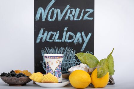 The holiday of Navruz. Traditional armudu tea Cup with national patterns and buta print. Two lemons with a branch, Turkish delight, black and white raisins in an old copper sugar bowl. On a black background plate with the inscription the holiday of Novruz and drawing Samani.の写真素材