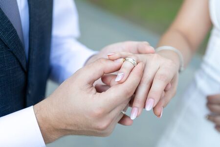 A man in a vest and tie wearing a gold wedding ring to a woman in a wedding dress on the ring finger.の写真素材