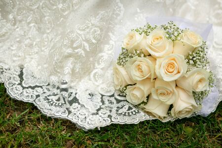 Wedding bouquet of white roses lying on a white wedding dress.の写真素材