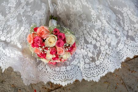 Wedding bouquet of colorful roses lying on a white wedding dress.の写真素材