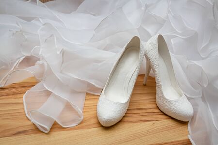 White, womens, wedding shoes with heels with patterns in the shape of flowers on the background of the wedding dress.の写真素材
