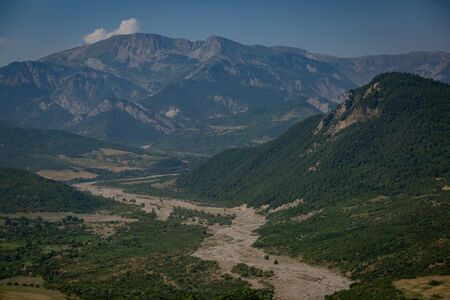 Riverbed between the hills overgrown with trees and vegetation on the background of a mountain range.の写真素材