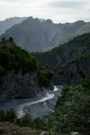 Riverbed between the hills, overgrown with trees and vegetation on the background of a mountain range.の写真素材