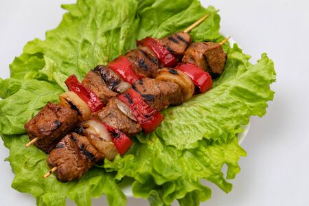 Pieces of fried meat and vegetables on skewers lying on a plate on a sheet of salad on a white background.の写真素材