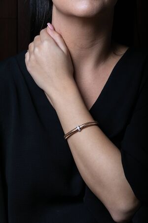Female, wicker, bracelet from rose gold with diamonds in the middle on woman hand, on black background.の写真素材
