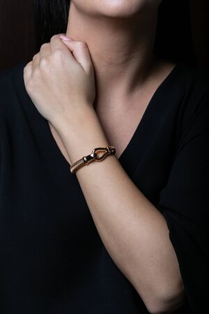 Female, wicker, bracelet from rose gold with carbine in the middle on woman hand, on black background.の写真素材