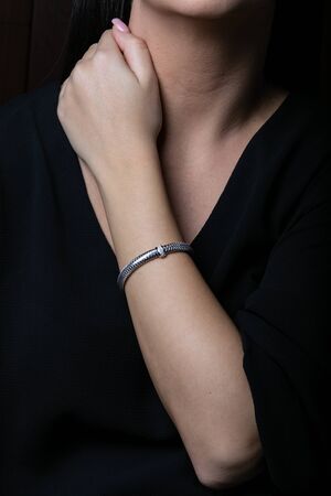 Female, silver, wicker, bracelet with diamonds in the middle on woman hand, on black background.の写真素材