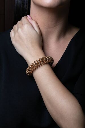 Female, rose gold wicker bracelet in the shape of a spring on hand, on a black background.の写真素材