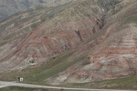 The road passing near the foot of the mountain covered with vegetation and red stripes.の写真素材