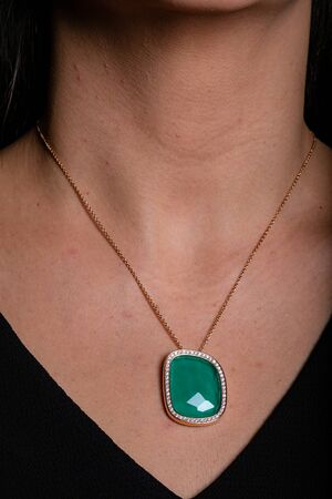 Gold women chain with a pendant, a green stone in the middle and a fringe of diamonds hanging around his neck.の写真素材