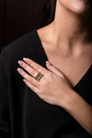 Female gold ring with stones on the edges on finger, on a black background.の写真素材