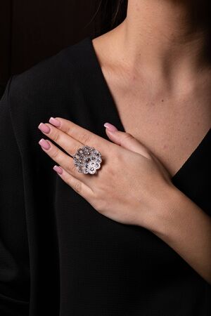 Women silver ring in the form of a big flower with diamonds on the finger, on a black background.の写真素材