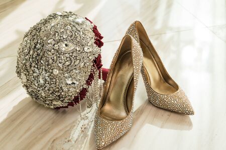Wedding bouquet and Golden shoes of the bride with stones on the floor of marble tiles.の写真素材