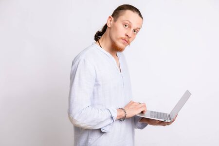 A guy in a light blue shirt holding a laptop in his hands, looking at the camera.の写真素材