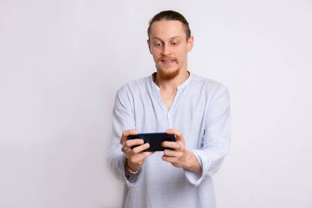 A guy in a light blue shirt playing a game on his phone.の写真素材
