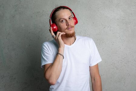 A guy in a white t shirt with red headphones on a gray background.の写真素材