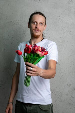 A guy in a white t shirt with red flowers smiling on a gray background.の写真素材