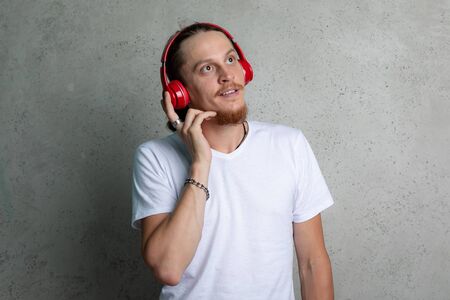 A guy in a white t shirt with red headphones dreaming on a gray background.の写真素材