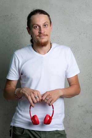 A guy in a white t shirt with red headphones in his hands on a gray background.の写真素材
