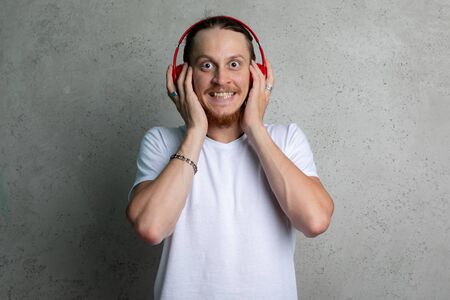 A guy in a white tshirt with red headphones smiling on a gray background.の写真素材
