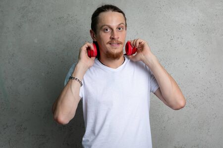 A guy in a white tshirt with red headphones on a gray background.の写真素材