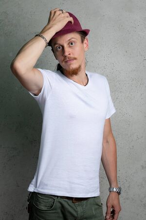 A guy in a white tshirt with a Burgundy hat, on a gray background.の写真素材