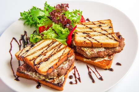 Hamburger closeup with bacon and cheese sauce with salad and olive dressing on on a white plate