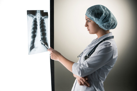Image of attractive woman doctor looking at x-ray results on a gray background