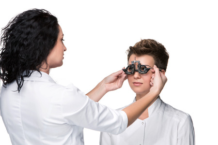 Optometrist holding an eye test glasses and giving to young woman eye examination. Isolate on white...