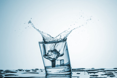 ice cube falling into a glass of water on blue backgroundの写真素材