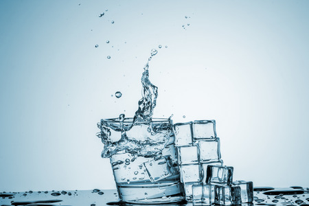 ice cubes falling into a glass of water and ice cubes, lying next, on blue backgroundの写真素材
