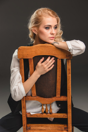 Beauty blond woman  in a black suit and white shirt, sitting on a chair on a gray backgroundの写真素材