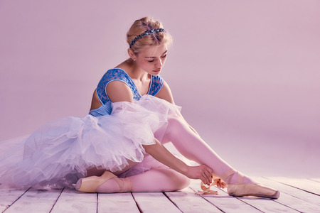 Professional ballerina putting on her ballet shoes on the wooden floor on a pink backgroundの写真素材